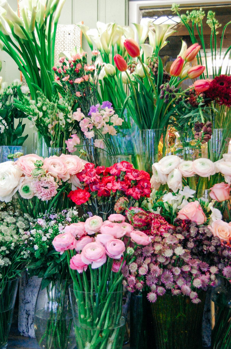 Frisch geschnittene Blumen in Vasen, darunter Lilien und Tulpen.