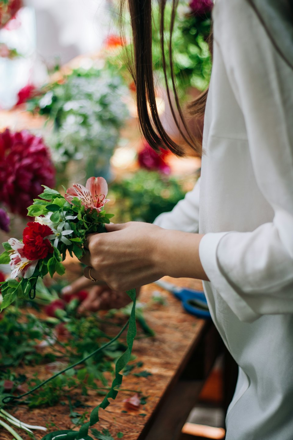 Hände arrangieren einen bunten Blumenstrauß mit grünem Laub.