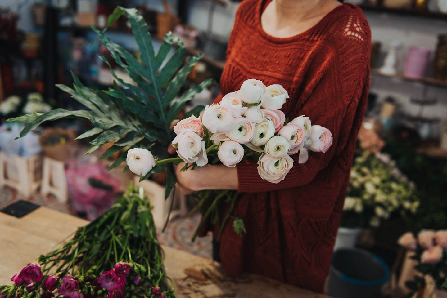 Person arrangiert rosa und weiße Ranunkelblumen an einer Holztheke.