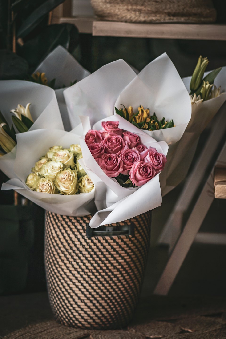 Frische Blumensträuße in weißem Papier stehen in einem geflochtenen Korb.